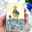 Load image into Gallery viewer, Notions Tin Firefly Notes featuring a duck in a raincoat with floral design, perfect for knitters and makers.
