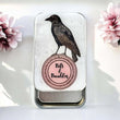 Load image into Gallery viewer, Notions Tin Firefly Notes featuring a crow design, labeled 'Bits &amp; Baubles', surrounded by flowers.
